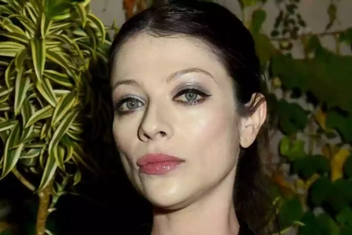 A person with pink eye and lip makeup, with plants in the background.