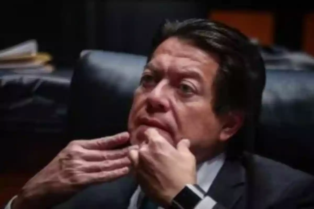 A man sitting in a dark armchair with his hands on his face and a pensive expression.