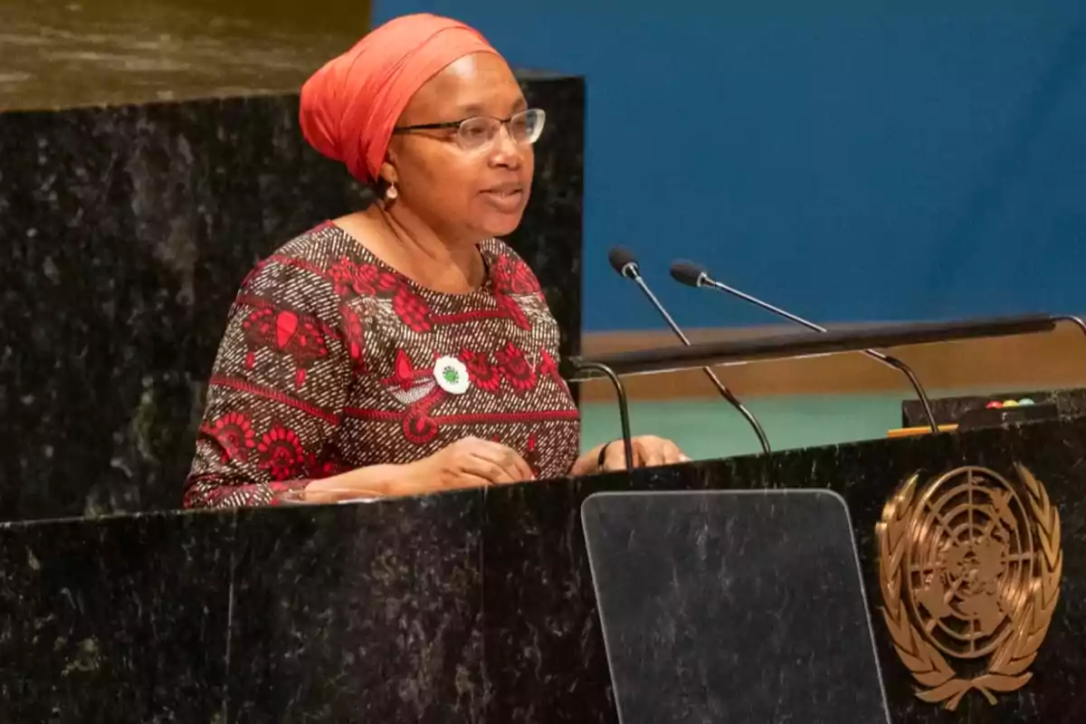 Una mujer con un turbante naranja y vestido estampado habla en un podio con el emblema de la ONU.