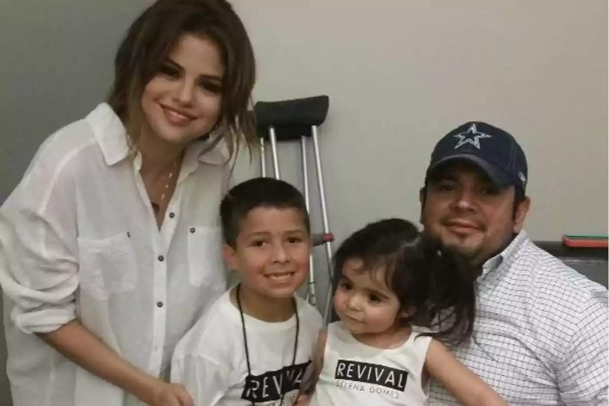 Un grupo de personas posando para una foto, incluyendo a una mujer con camisa blanca, un hombre con gorra y dos niños pequeños.