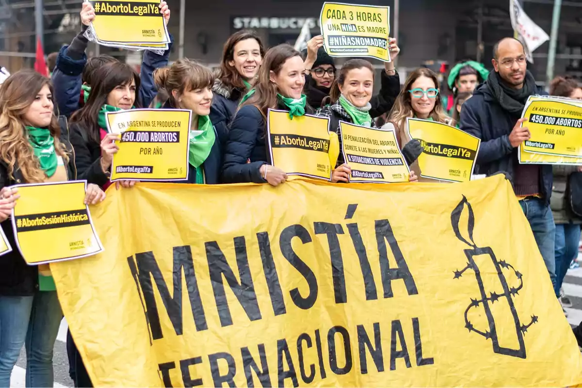 Un grupo de personas sostiene pancartas amarillas y verdes en una manifestación a favor del aborto legal en Argentina, con un cartel grande de Amnistía Internacional.