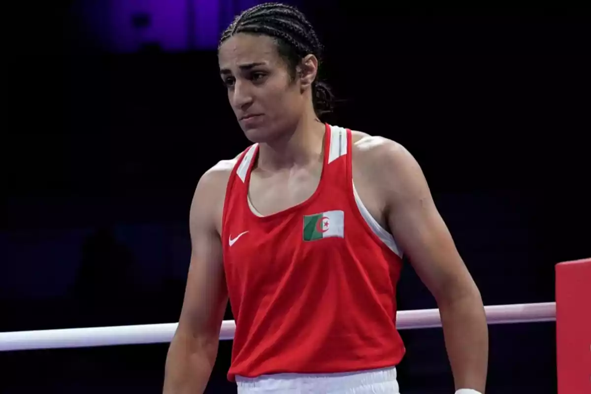 Una boxeadora con uniforme rojo y una bandera en el pecho está en el ring.