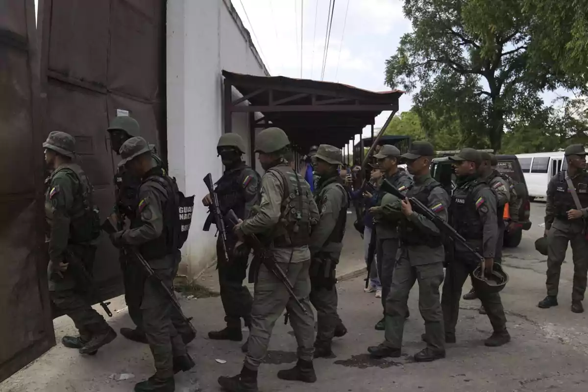 Un grupo de soldados con uniformes verdes y armas largas entra por una puerta metálica en un edificio blanco.