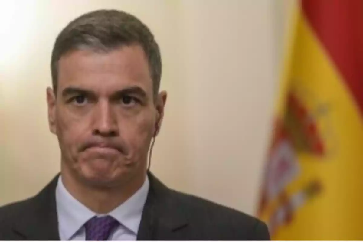 Un hombre con expresión seria frente a una bandera de España.