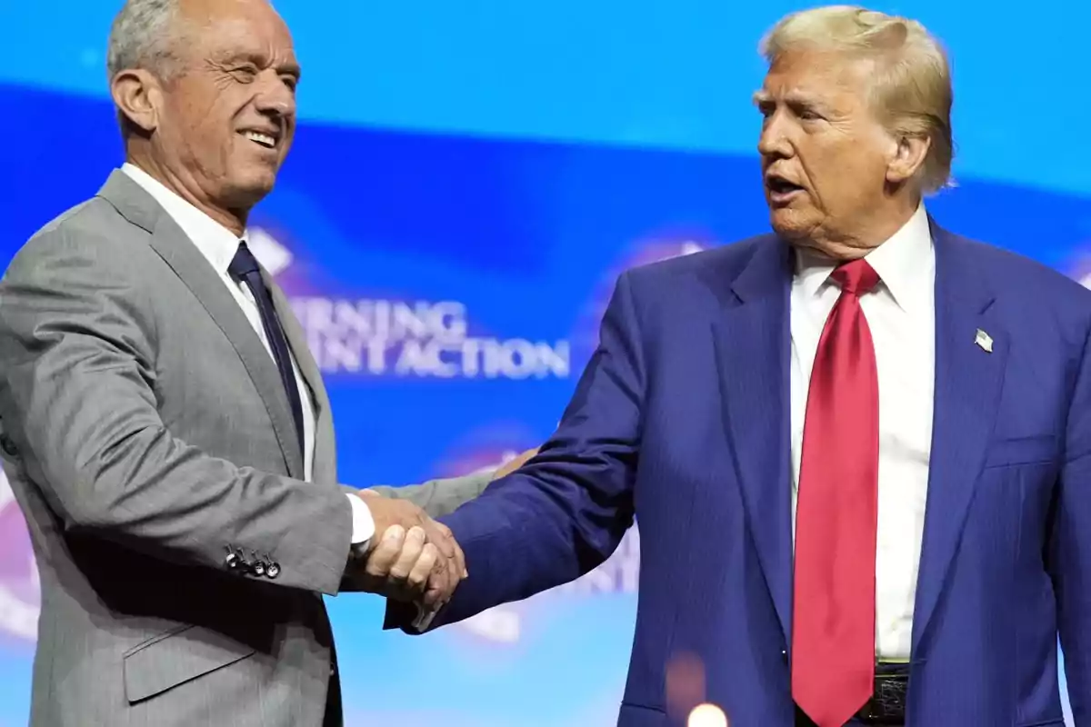 Two men in suits shaking hands on a stage with a blue background.