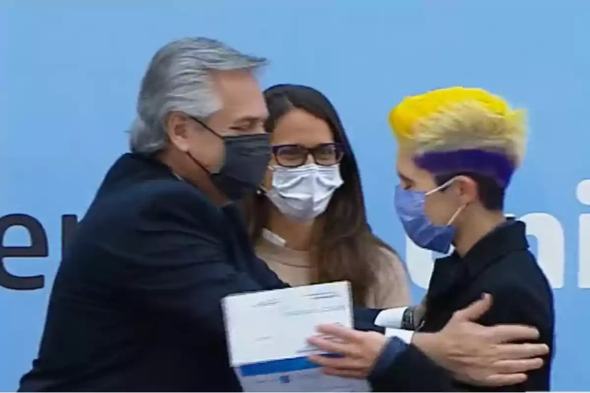 Tres personas con mascarillas se saludan y entregan un documento en un evento formal.