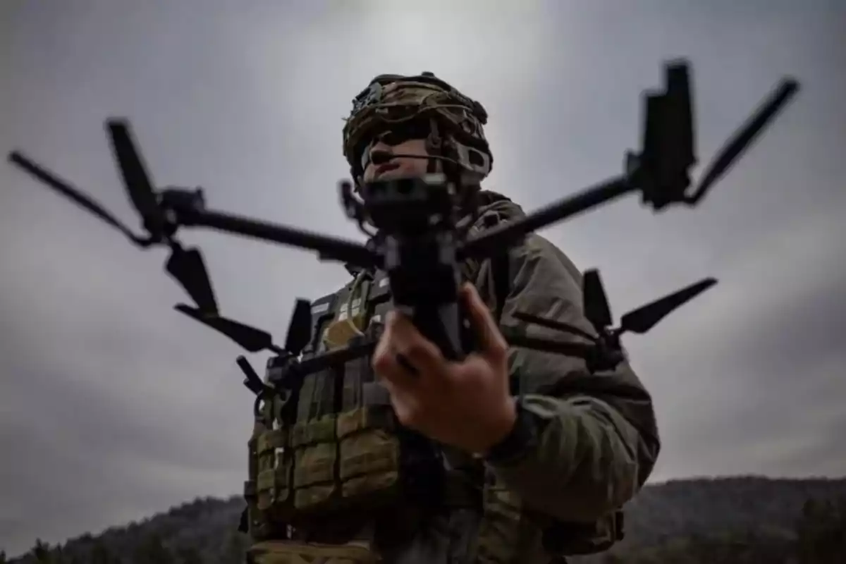 A soldier holding a drone in an outdoor setting with a cloudy sky.