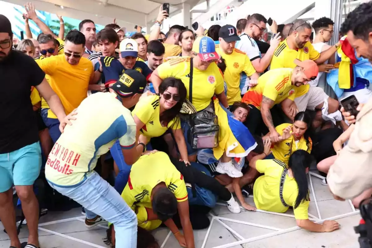 Un grupo de personas con camisetas amarillas se aglomera en un espacio reducido, algunos parecen estar cayendo o empujándose mientras otros observan o intentan ayudar.