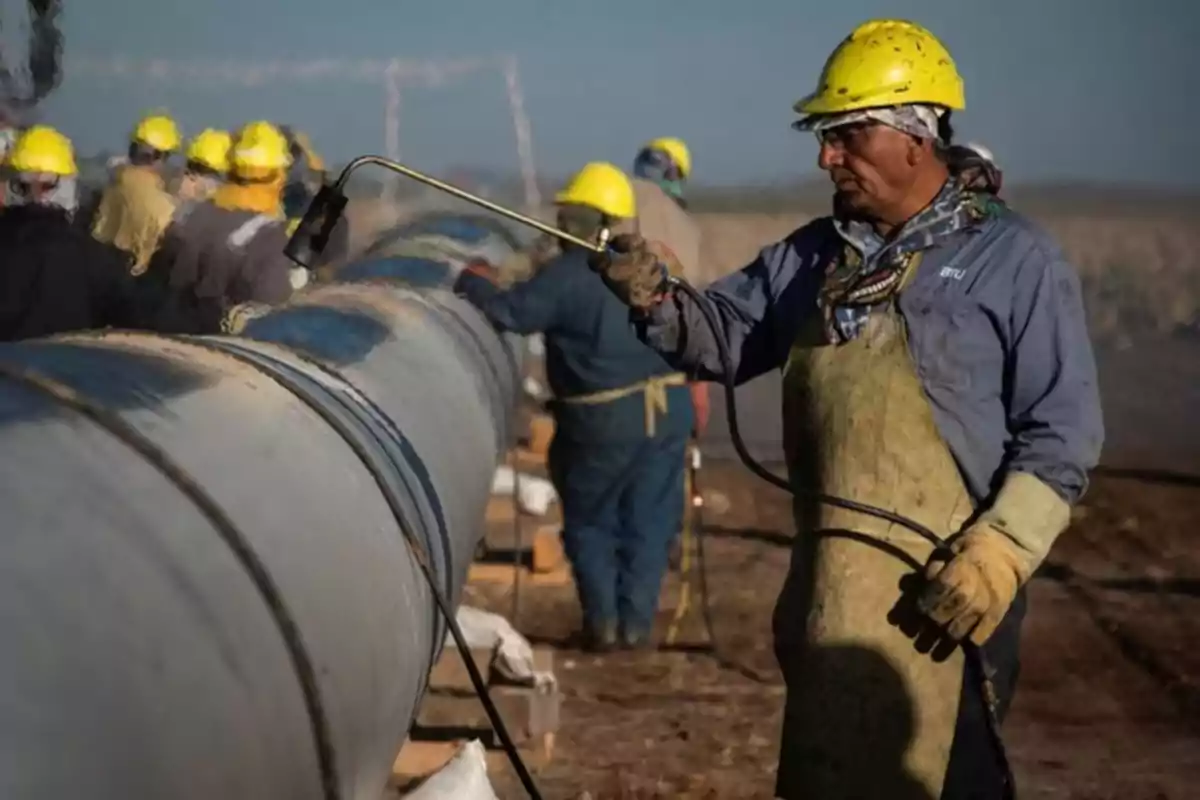 Trabajadores con cascos amarillos pintando un gasoducto en un sitio de construcción.