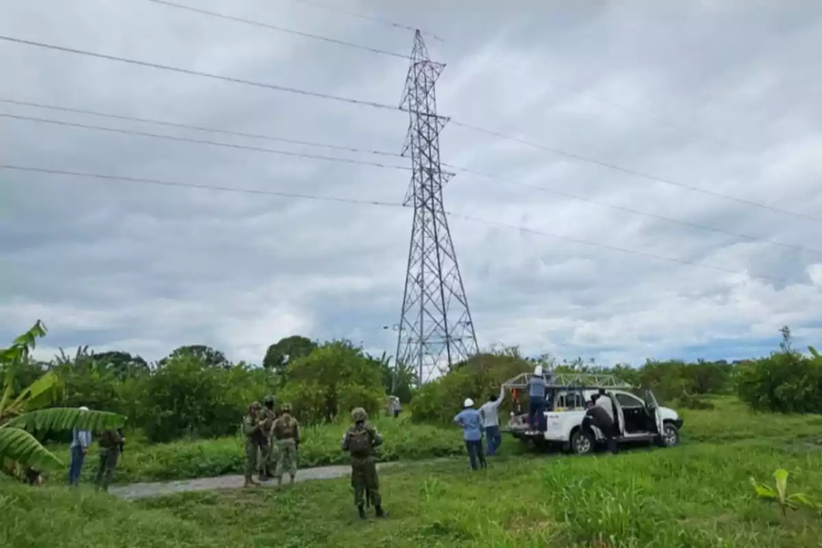 Personas y un vehículo cerca de una torre de electricidad en un área verde.