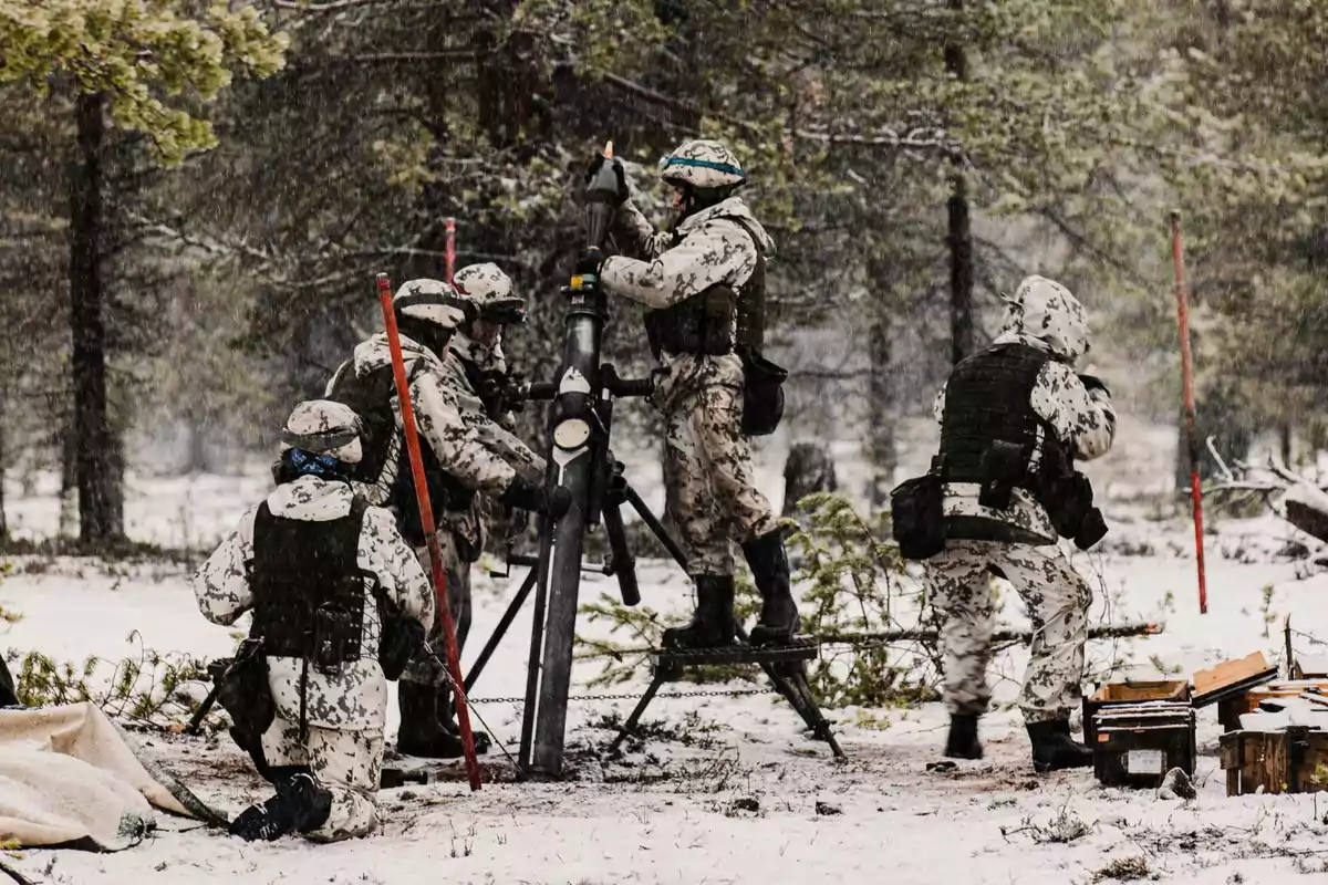 Soldados en uniforme de camuflaje invernal operan un mortero en un bosque nevado.