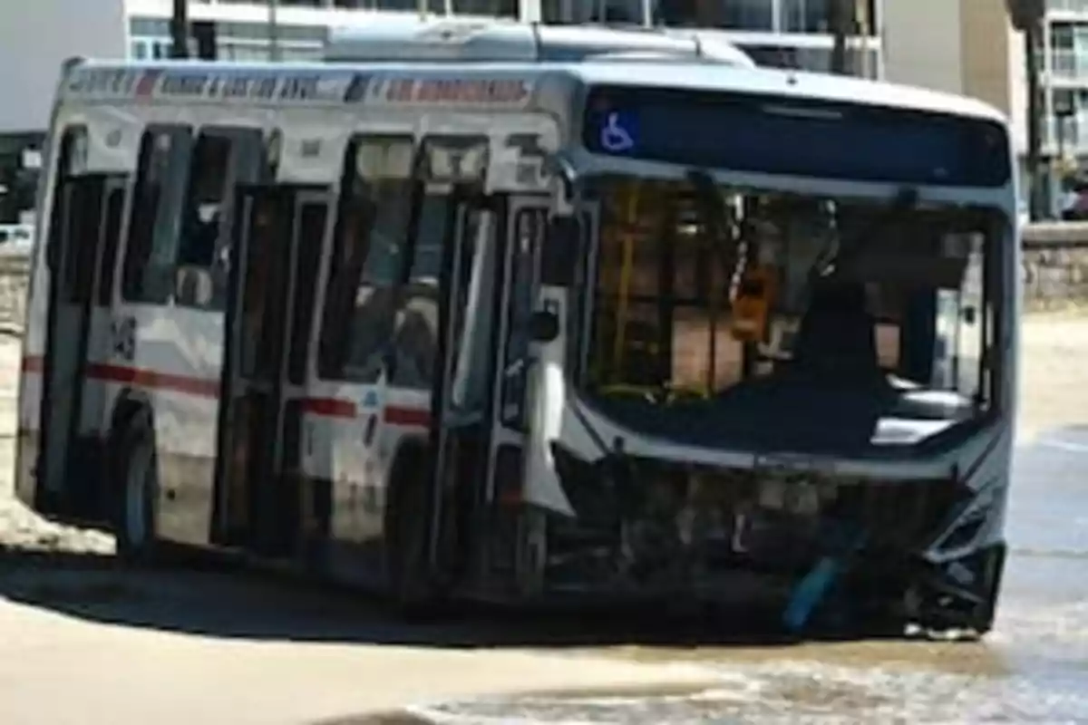 Un autobús accidentado en la playa con el frente dañado y parcialmente sumergido en el agua.