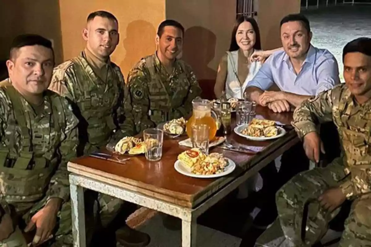 Un grupo de personas, algunas con uniforme militar, sentadas alrededor de una mesa con platos de comida y bebidas.