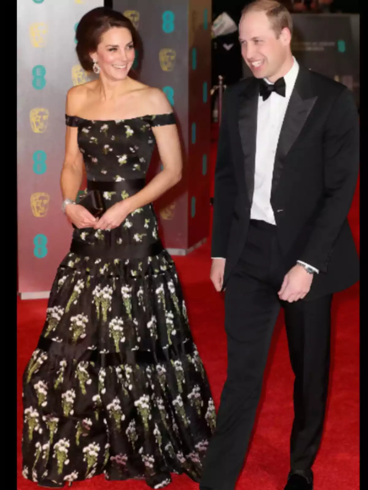 Una pareja elegantemente vestida camina por una alfombra roja en un evento formal.