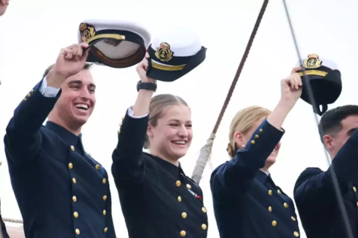 Personas en uniforme naval levantando sus gorras y sonriendo.