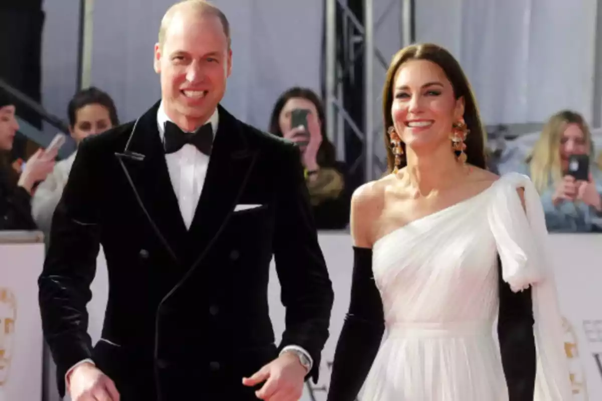 Dos personas elegantemente vestidas caminan por una alfombra roja rodeadas de fotógrafos y asistentes.