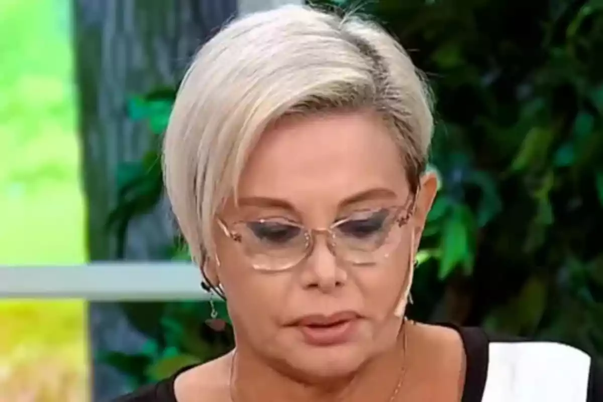 Una persona con cabello corto y rubio usando gafas transparentes en un entorno con fondo verde.