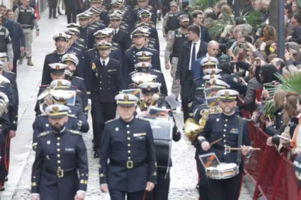 Un desfile de una banda militar marchando por una calle rodeada de espectadores.