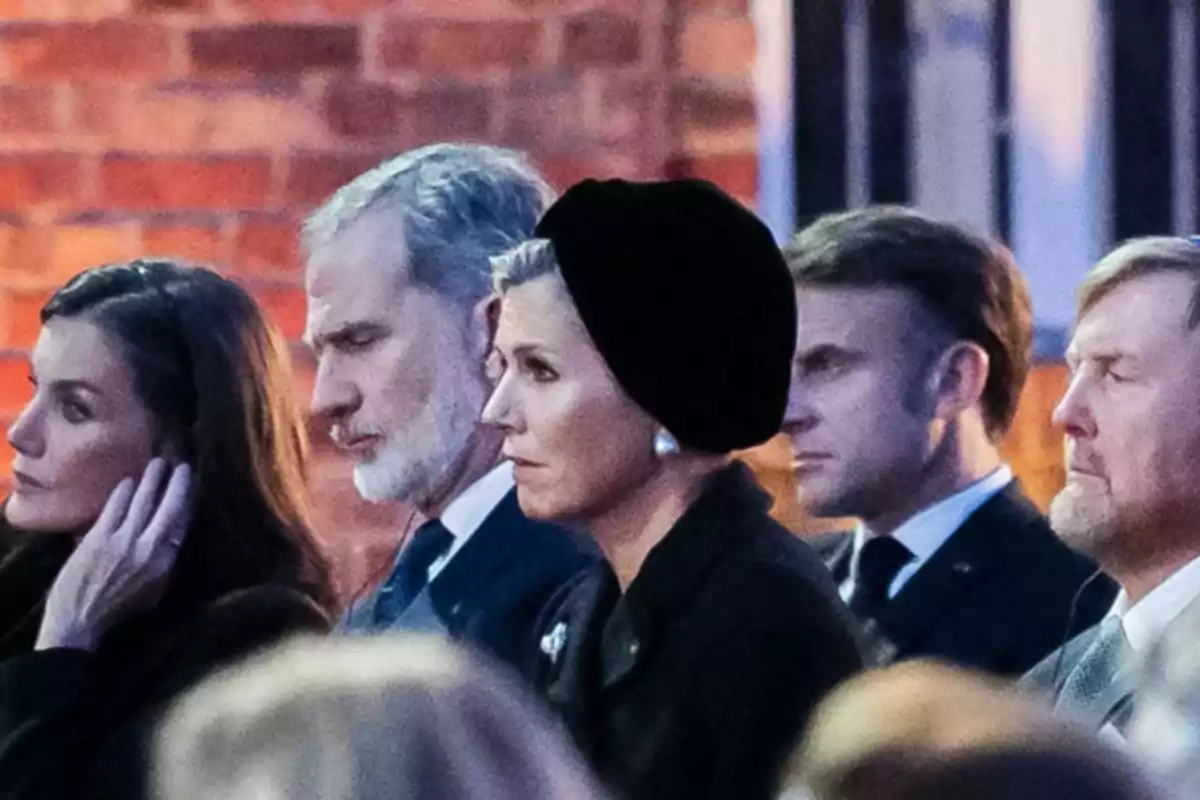 Un grupo de personas sentadas en un evento formal, con expresiones serias y vestimenta elegante.