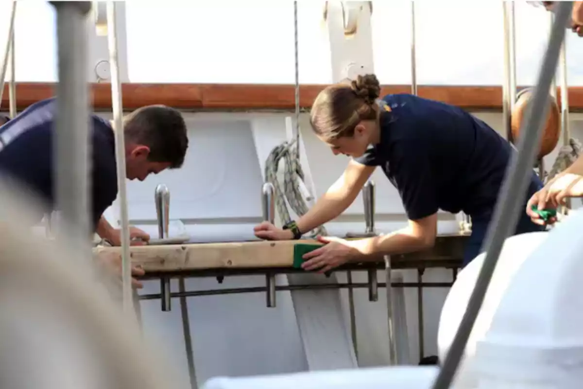 Personas trabajando en la cubierta de un barco, limpiando o puliendo una superficie de madera.