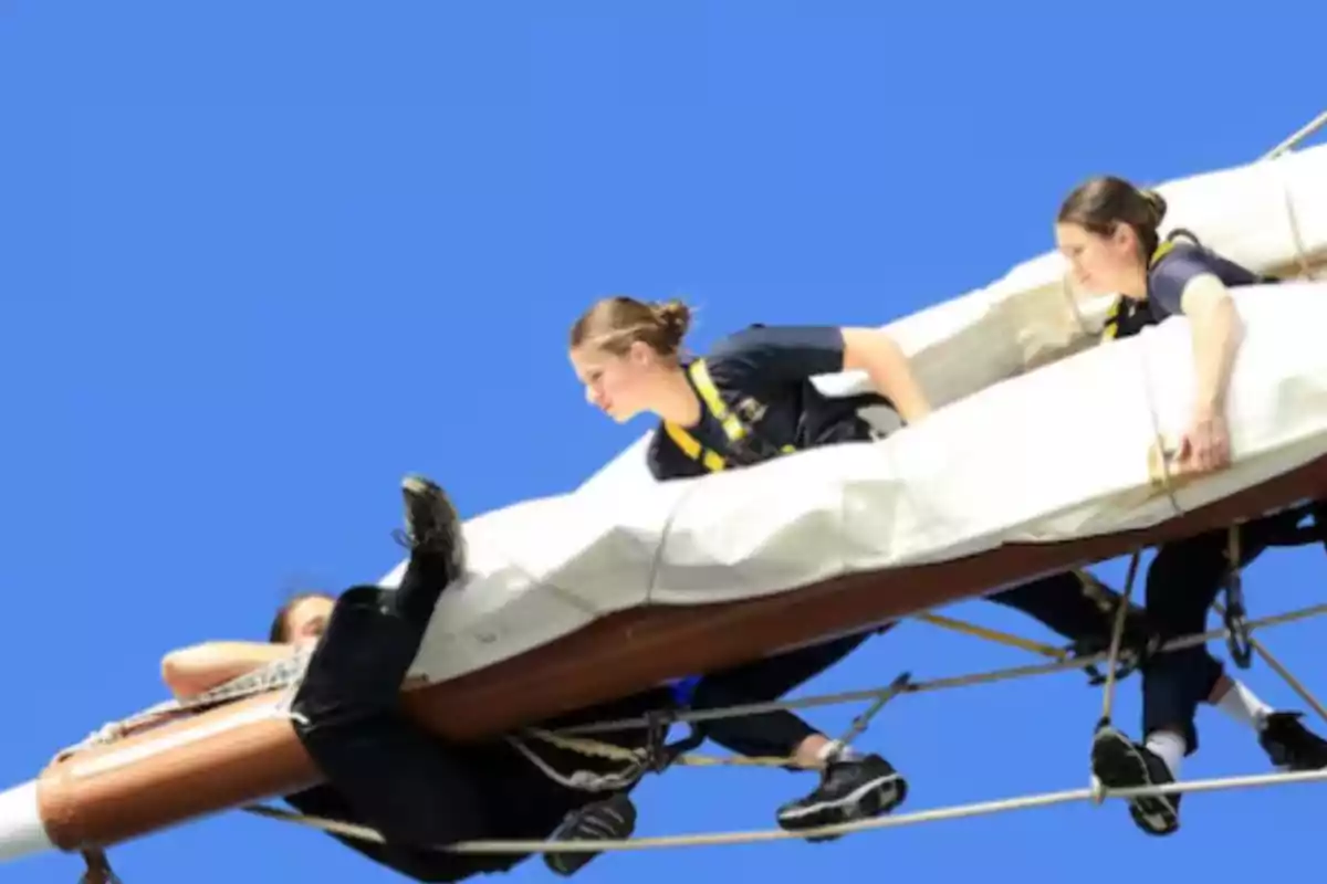 Personas trabajando en el aparejo de un barco bajo un cielo azul.