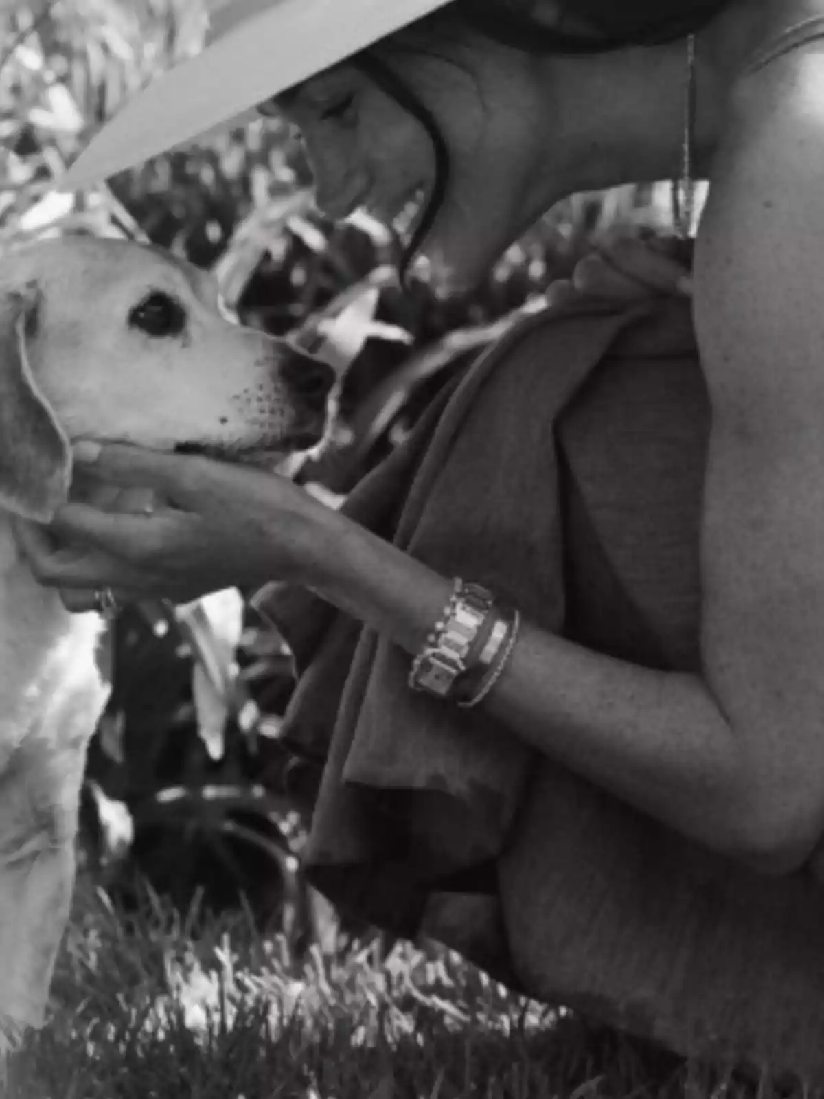 Una mujer sonriente con sombrero acaricia a un perro en un jardín.