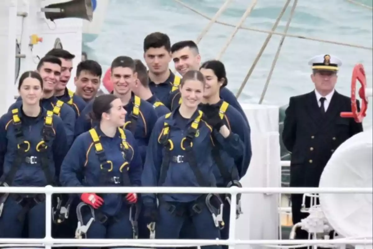 Un grupo de jóvenes con uniformes y arneses de seguridad sonríe en la cubierta de un barco mientras un oficial los observa.