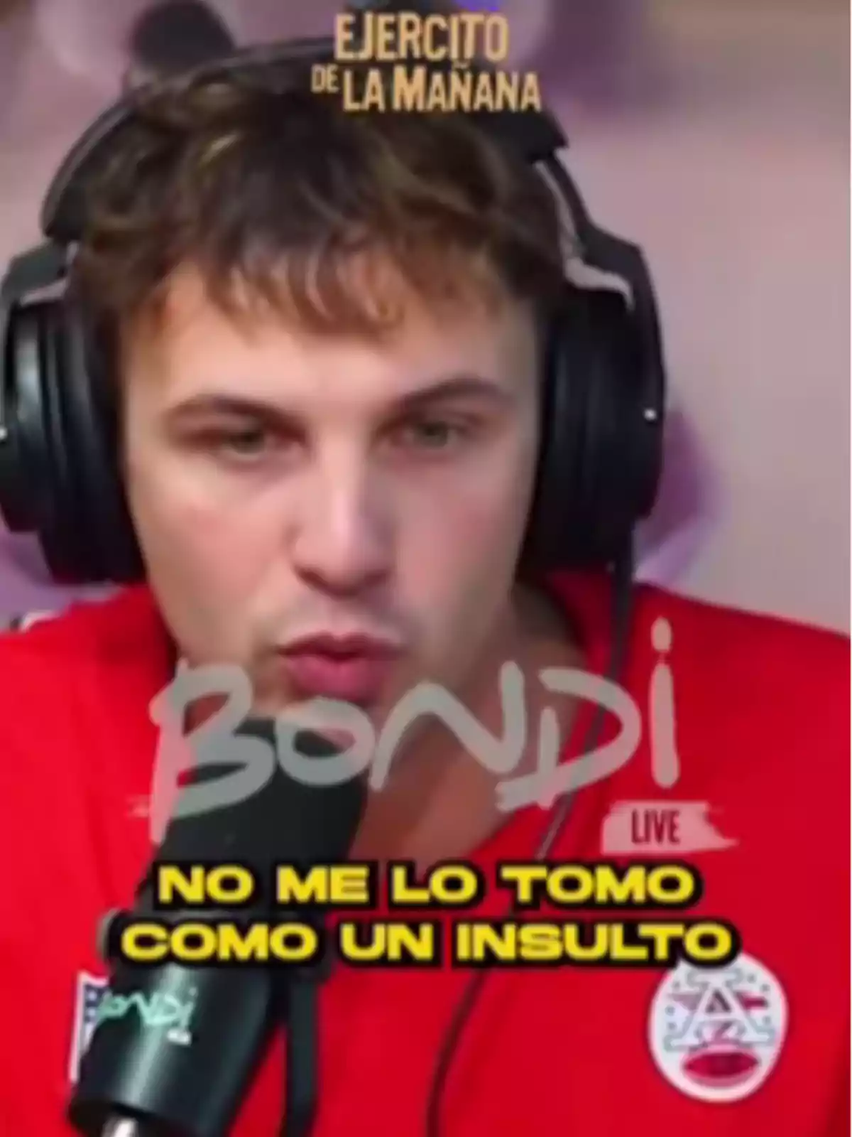 Un hombre con auriculares y camiseta roja habla frente a un micrófono con texto superpuesto que dice 