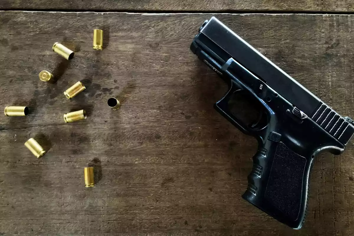 Una pistola negra junto a varias casquillos de bala sobre una superficie de madera.