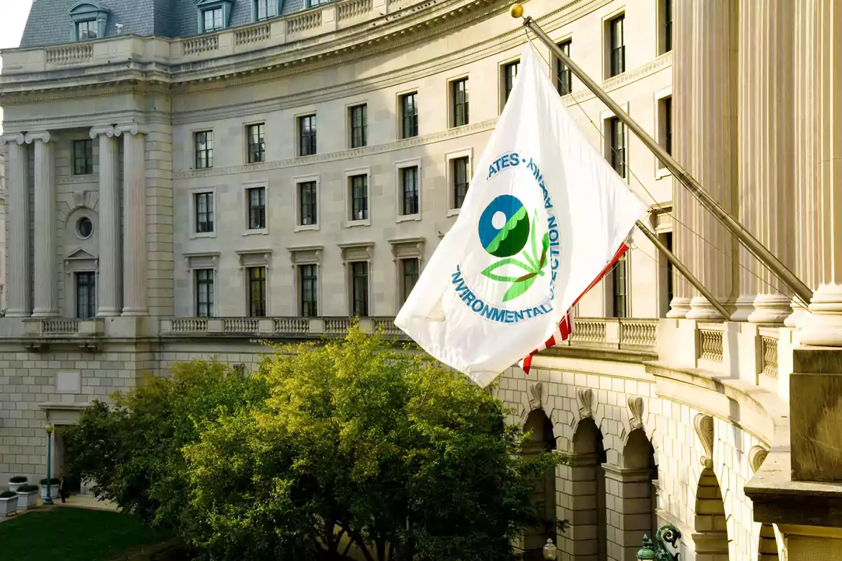 Bandera de una agencia ambiental ondeando frente a un edificio gubernamental clásico.