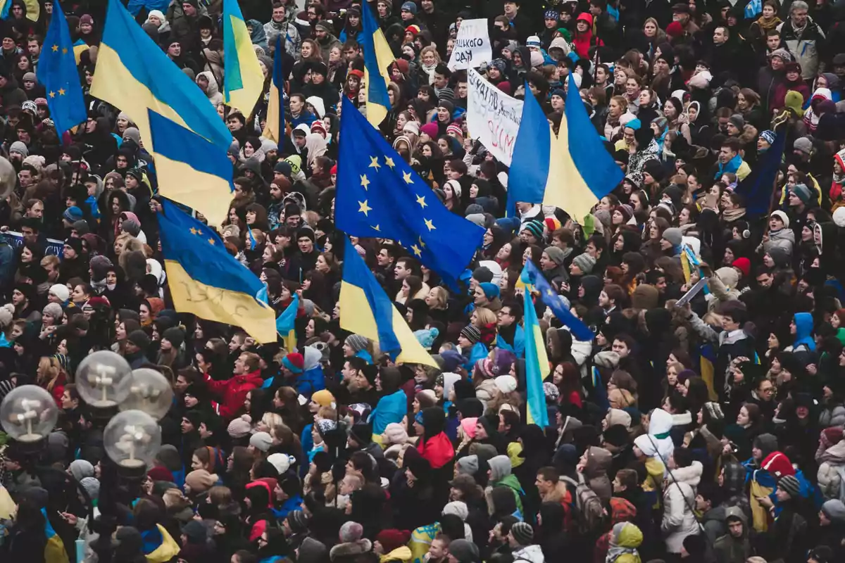 Una multitud de personas en una manifestación sosteniendo banderas de Ucrania y de la Unión Europea.