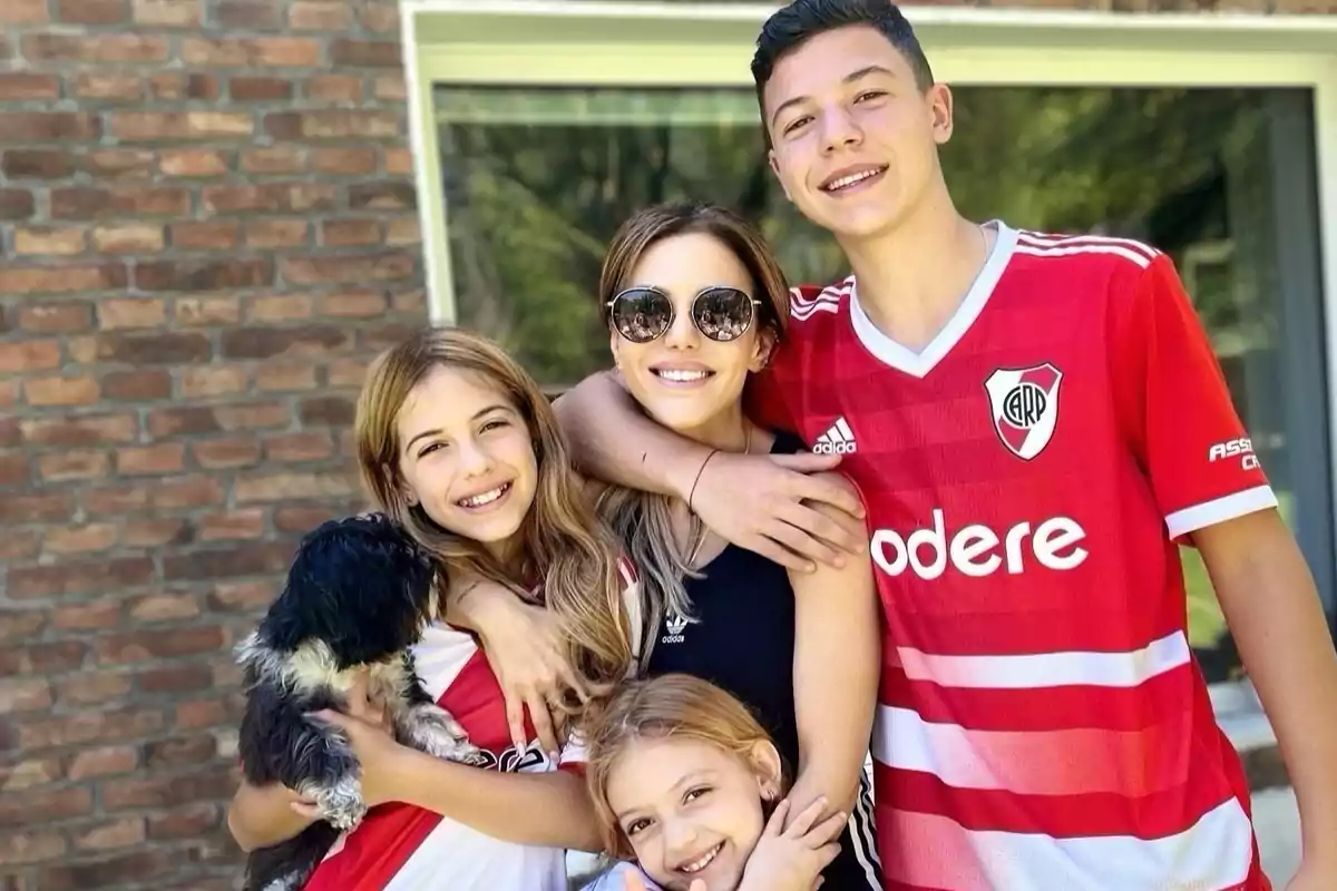 Una familia sonriente posando al aire libre con camisetas de fútbol y un perro pequeño.