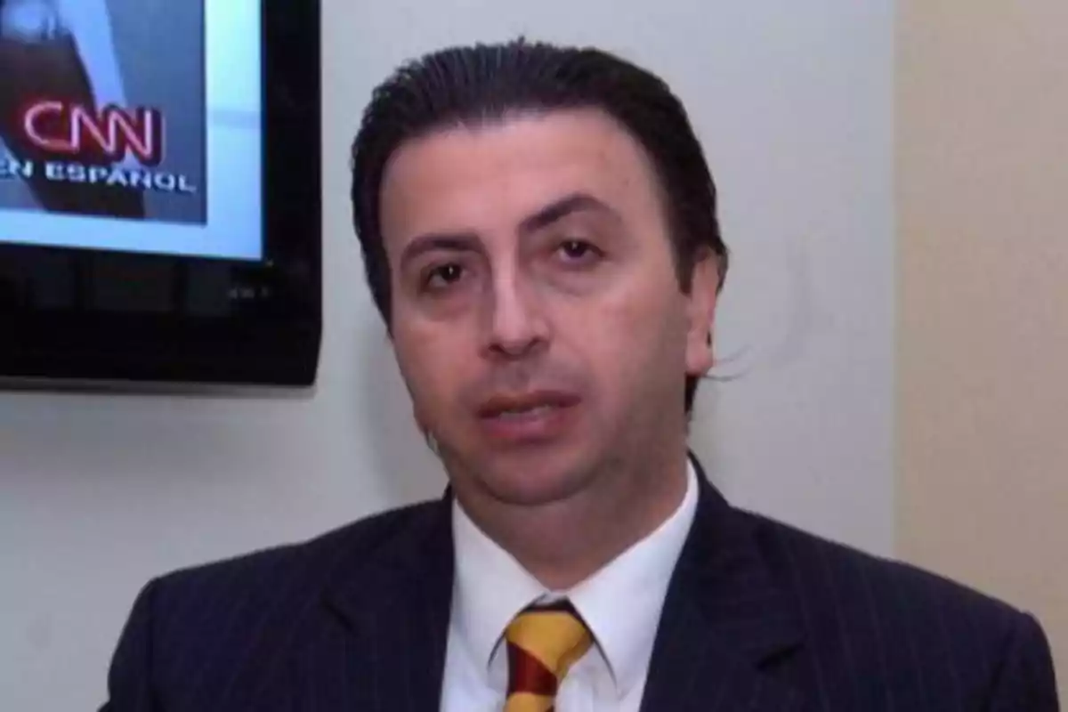 A man in a suit and tie in front of a television screen.