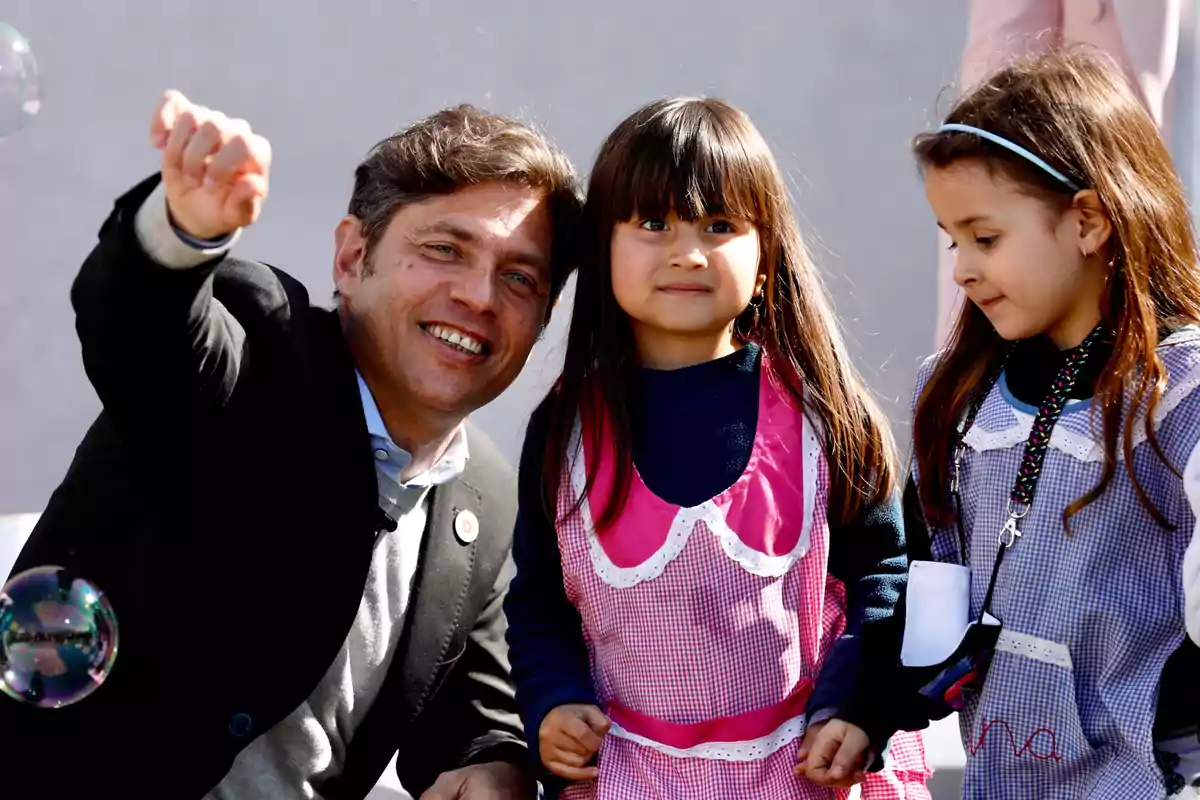 Un hombre sonriente junto a dos niñas pequeñas que llevan delantales coloridos.