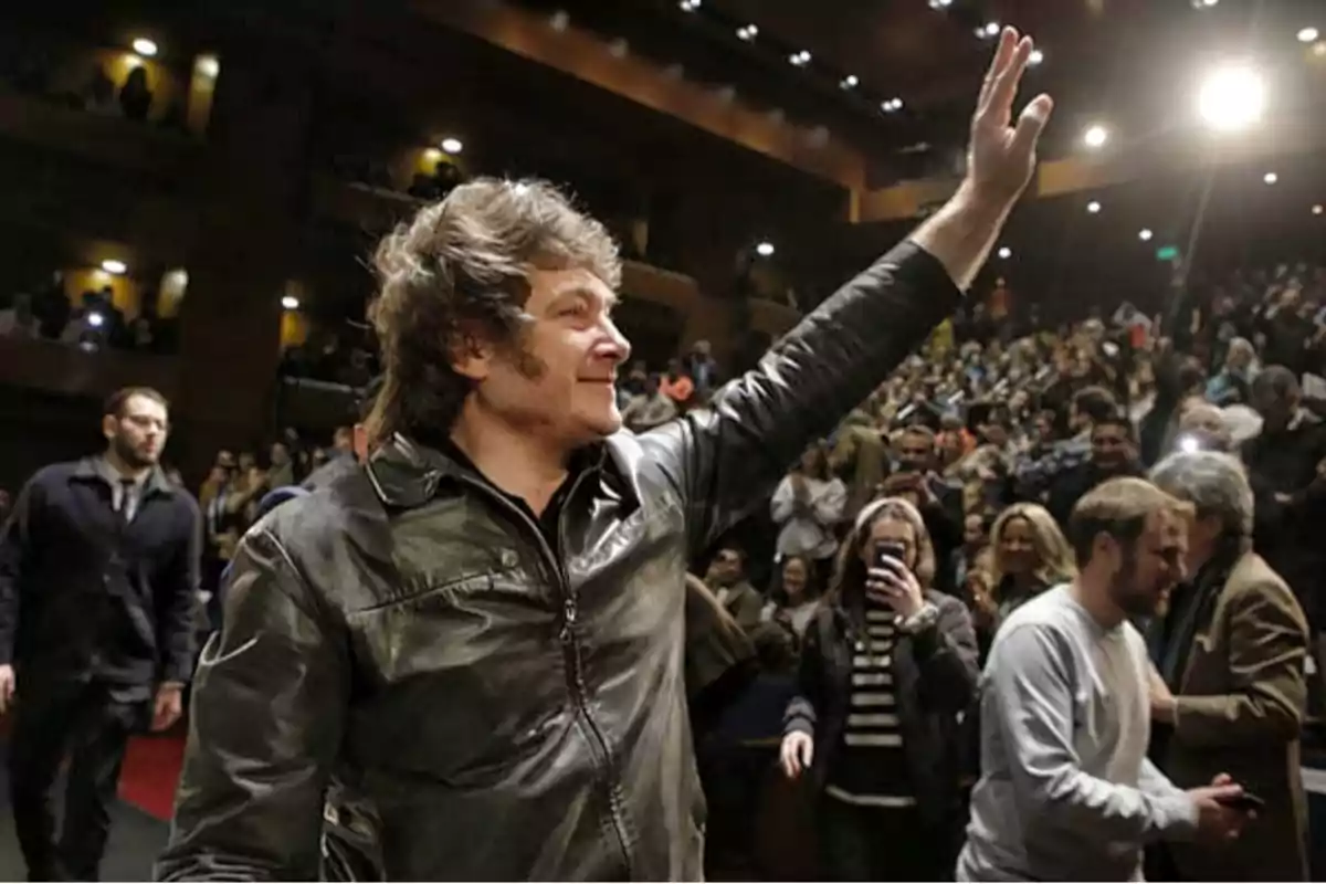 Un hombre con chaqueta de cuero levanta la mano en un auditorio lleno de gente.