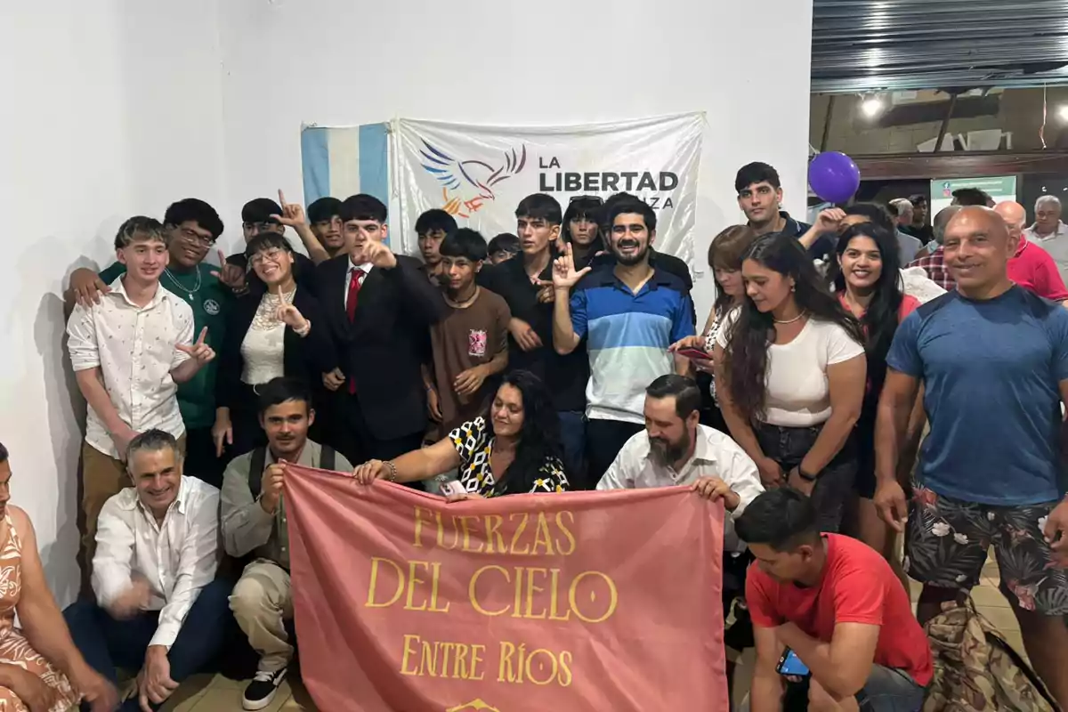 Un grupo de personas posando para una foto, algunas de ellas sostienen una pancarta que dice "Fuerzas del Cielo Entre Ríos", y al fondo hay una bandera con el texto "La Libertad Avanza".