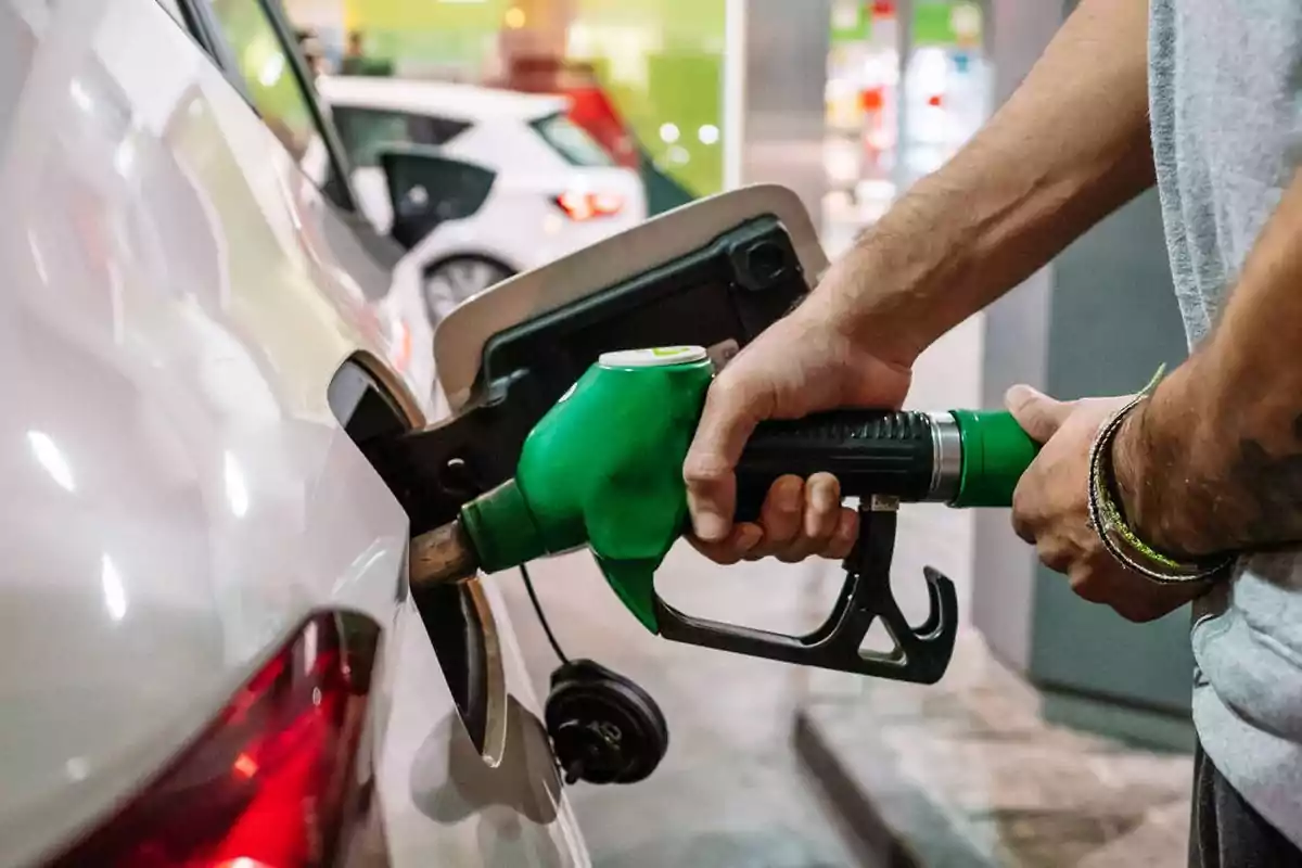 Persona llenando el tanque de un automóvil con una manguera de combustible verde en una estación de servicio.