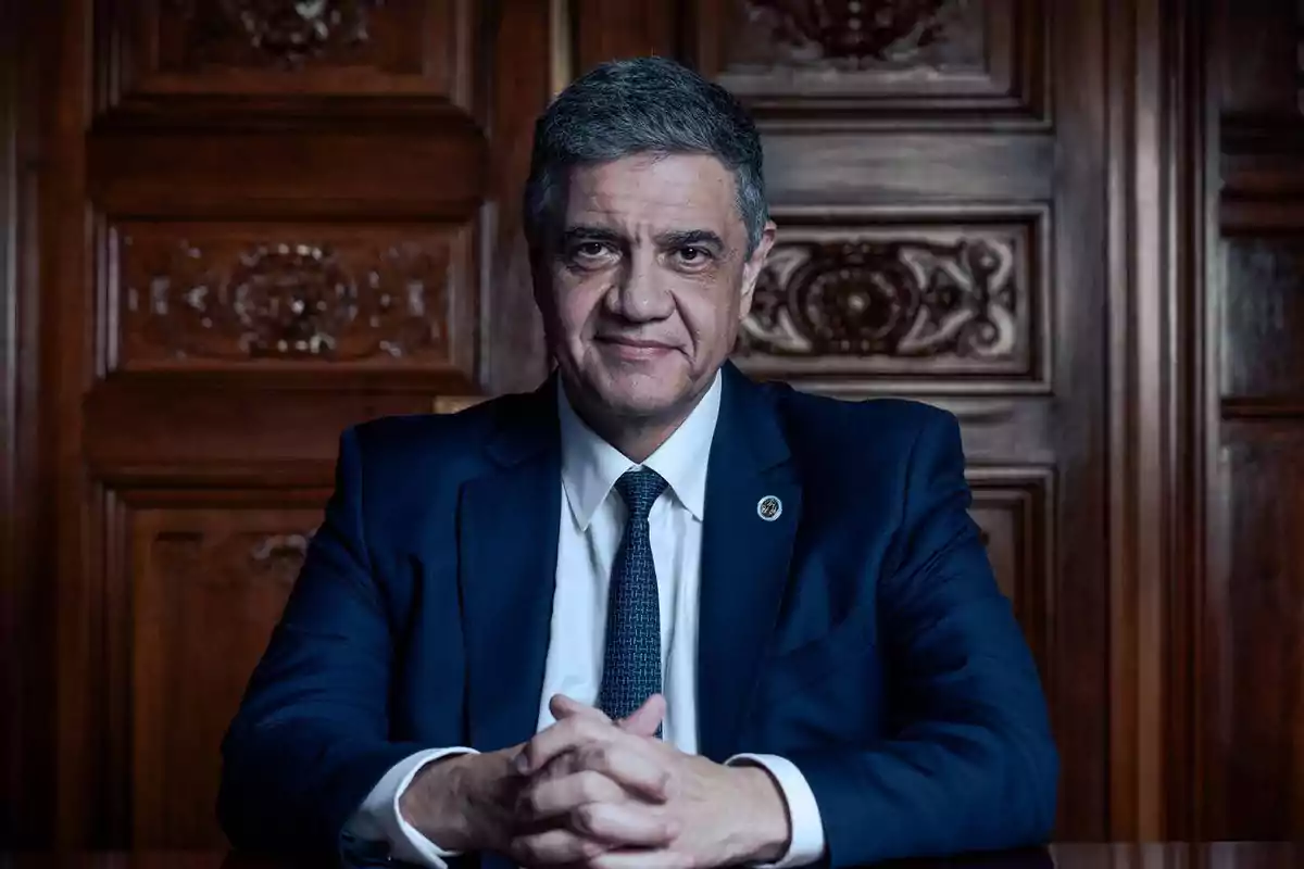 A man in a dark suit and tie poses in front of a carved wooden door.