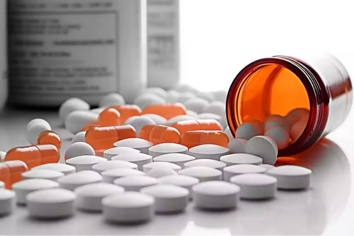 A jar of pills tipped over with orange capsules and white tablets scattered on a white surface.