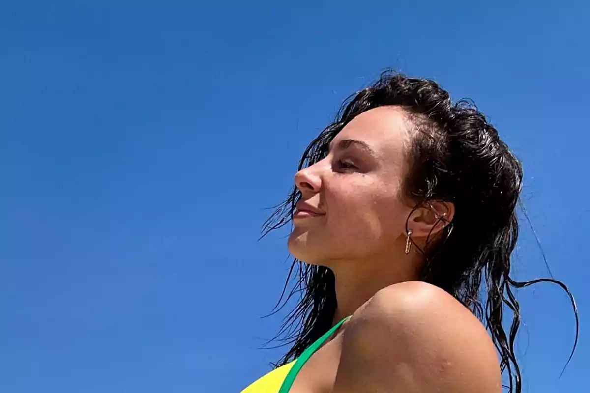 Mujer de perfil con el cabello mojado disfrutando del sol bajo un cielo azul.