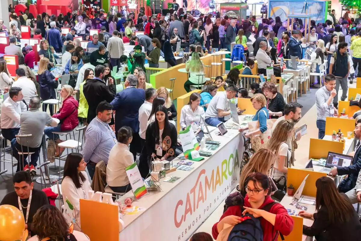 Una feria concurrida con muchas personas interactuando en diferentes stands, destacando uno con el letrero de Catamarca.