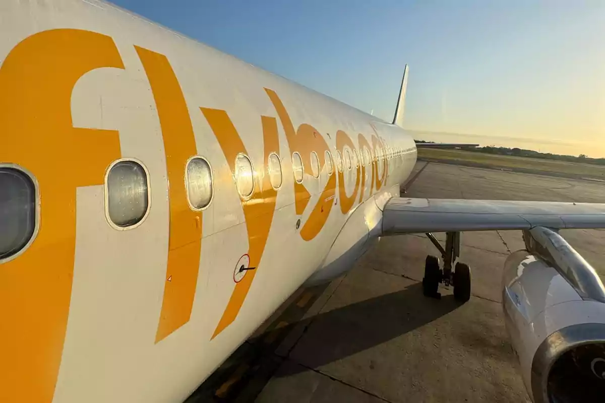 Un avión de la aerolínea Flybondi estacionado en la pista de un aeropuerto al atardecer.