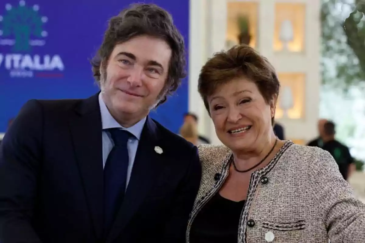 Dos personas sonriendo en un evento con fondo azul y decoración interior.