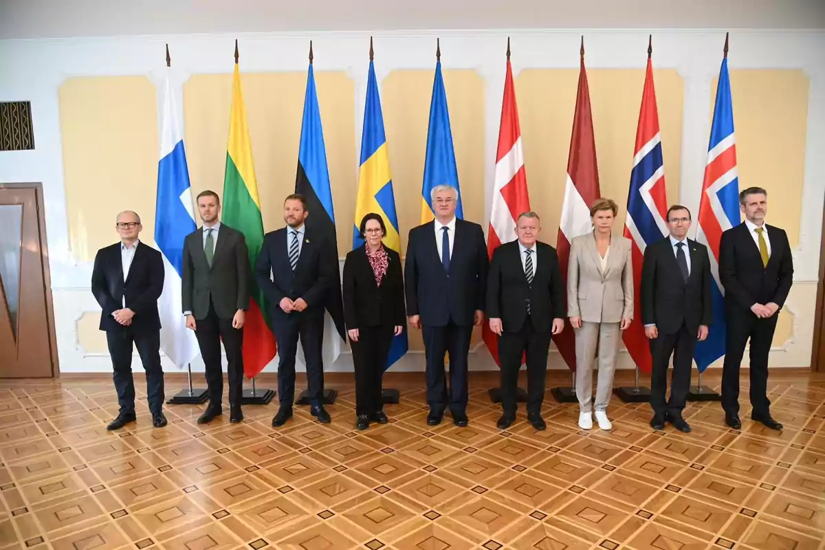 Un grupo de personas posando frente a una fila de banderas nacionales en una sala con piso de madera.