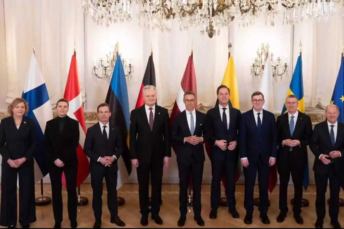 Un grupo de personas posando frente a varias banderas nacionales en una sala con candelabros.