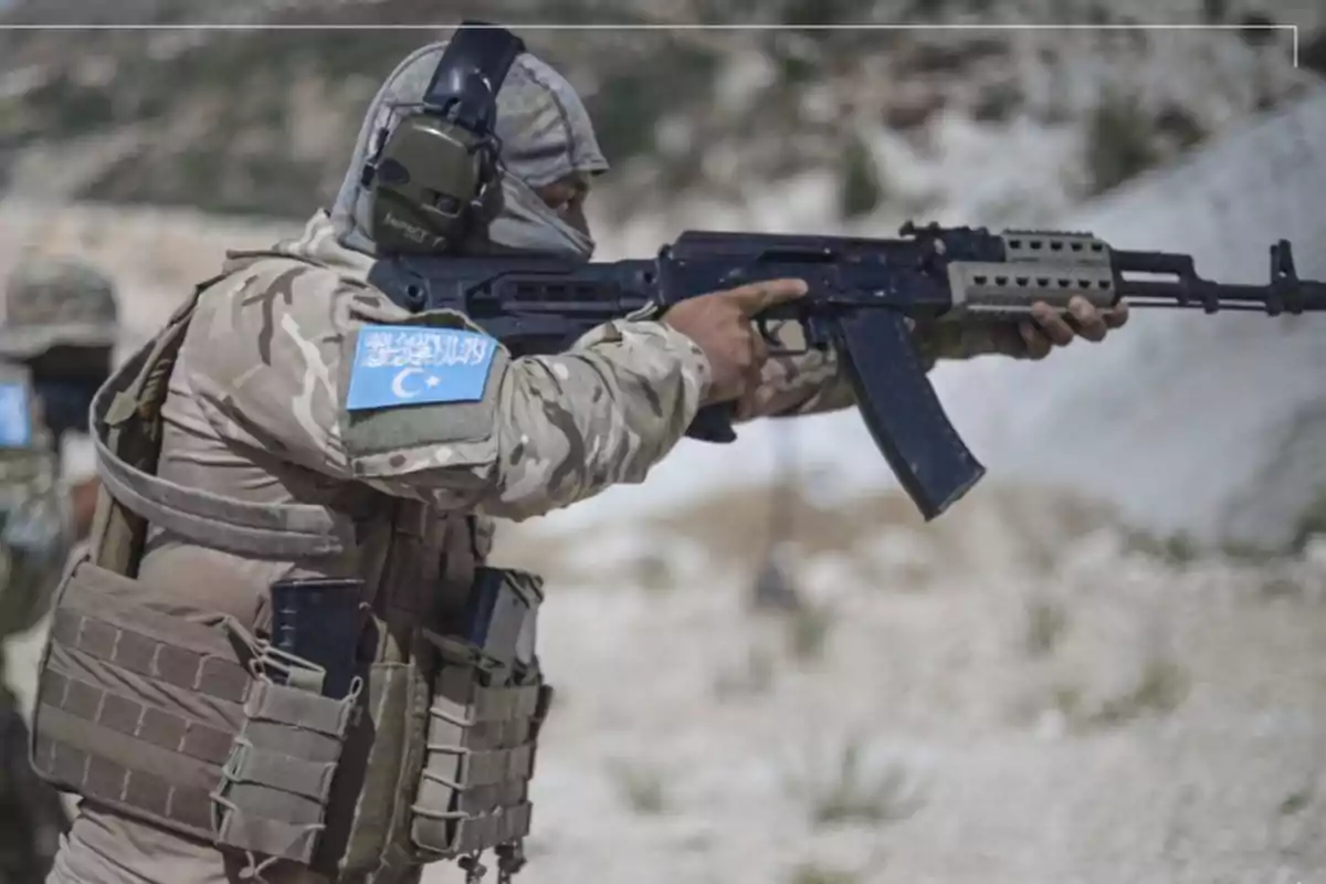 Un soldado en uniforme de camuflaje apunta un rifle en un entorno al aire libre.