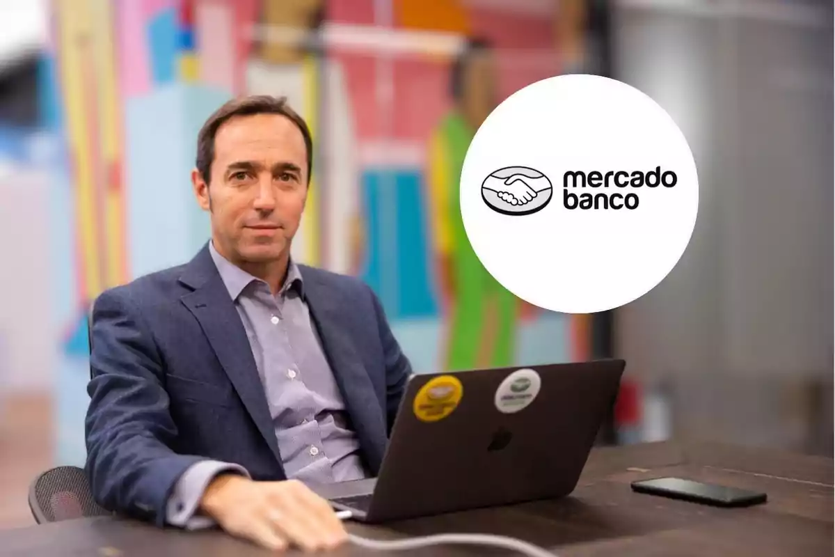 Un hombre en traje sentado frente a una computadora portátil con el logo de "mercado banco" en el fondo.