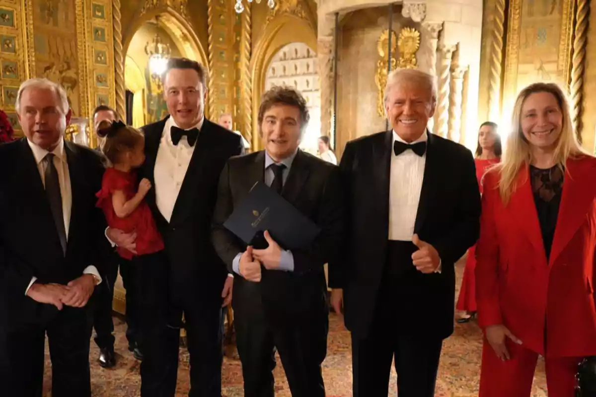 Un grupo de personas vestidas de manera formal posando en un elegante salón decorado con detalles dorados.