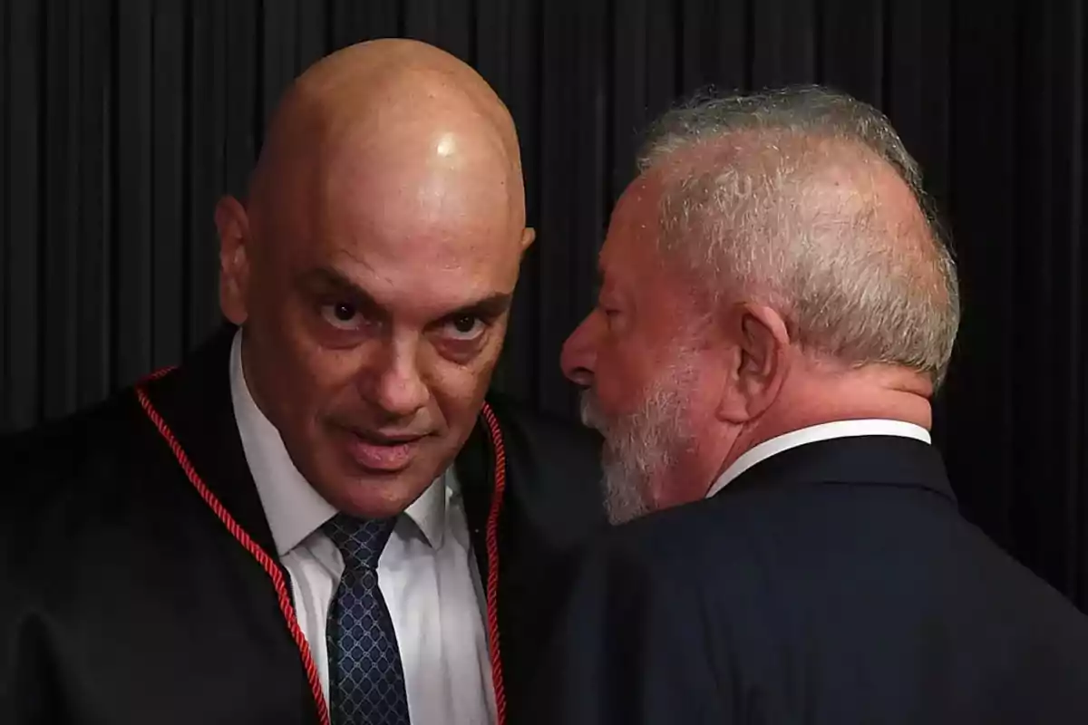 Dos hombres conversando en un evento formal, uno de ellos con toga y corbata.