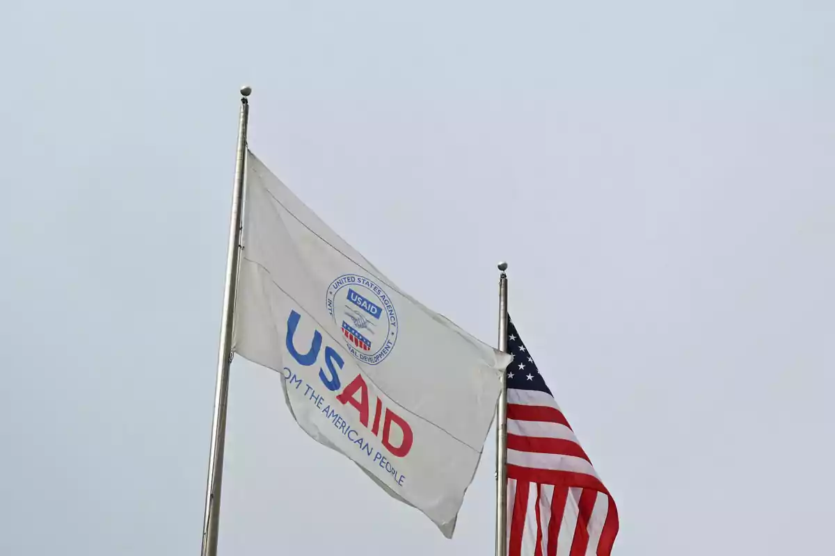 Dos banderas ondeando, una de USAID y otra de Estados Unidos, en un cielo nublado.